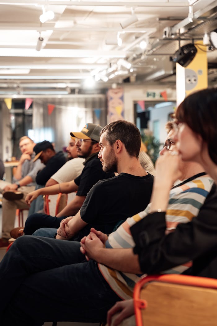 About A group of diverse adults attentively listening in a casual indoor event setting.