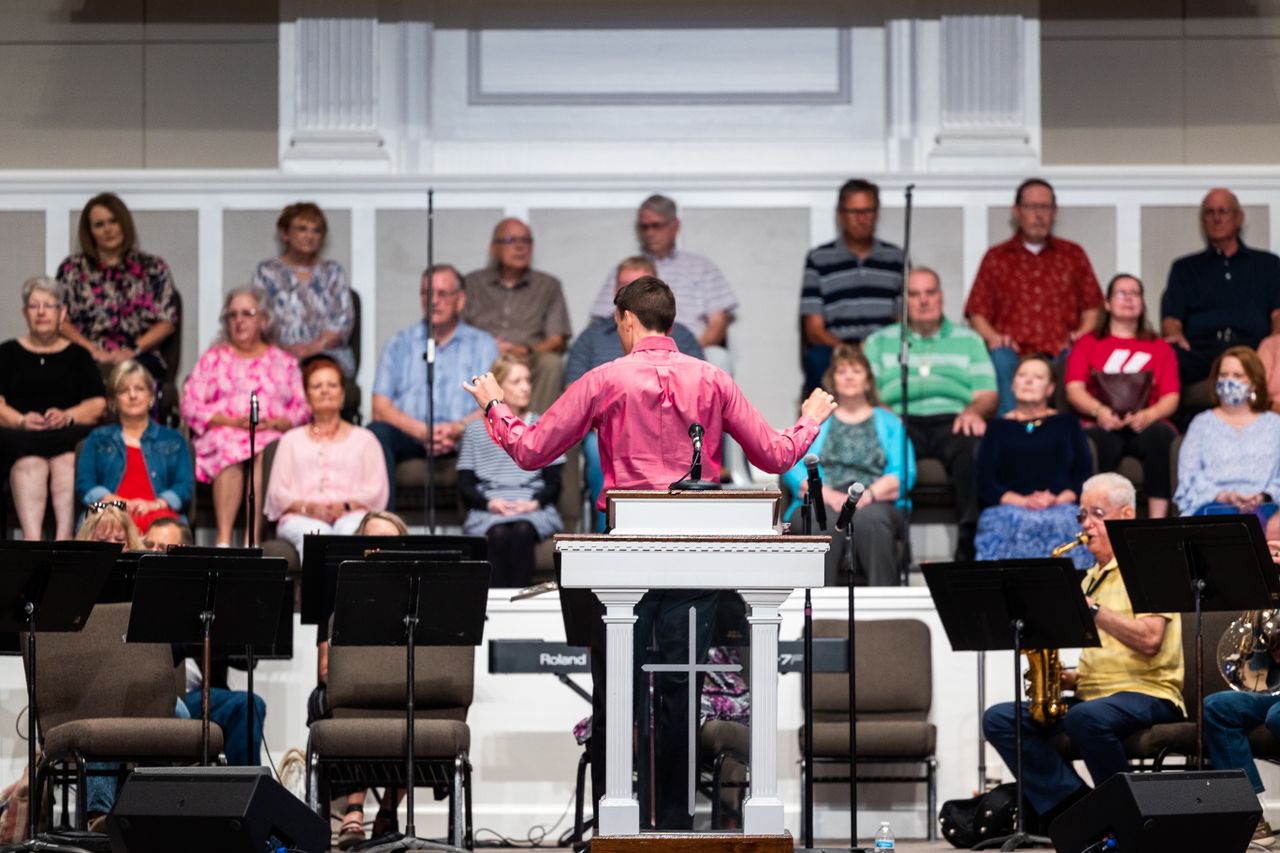 Crafting Captivating Headlines: Your awesome post title goes here A male conductor leads a choir rehearsal with a group of adults in a church setting.