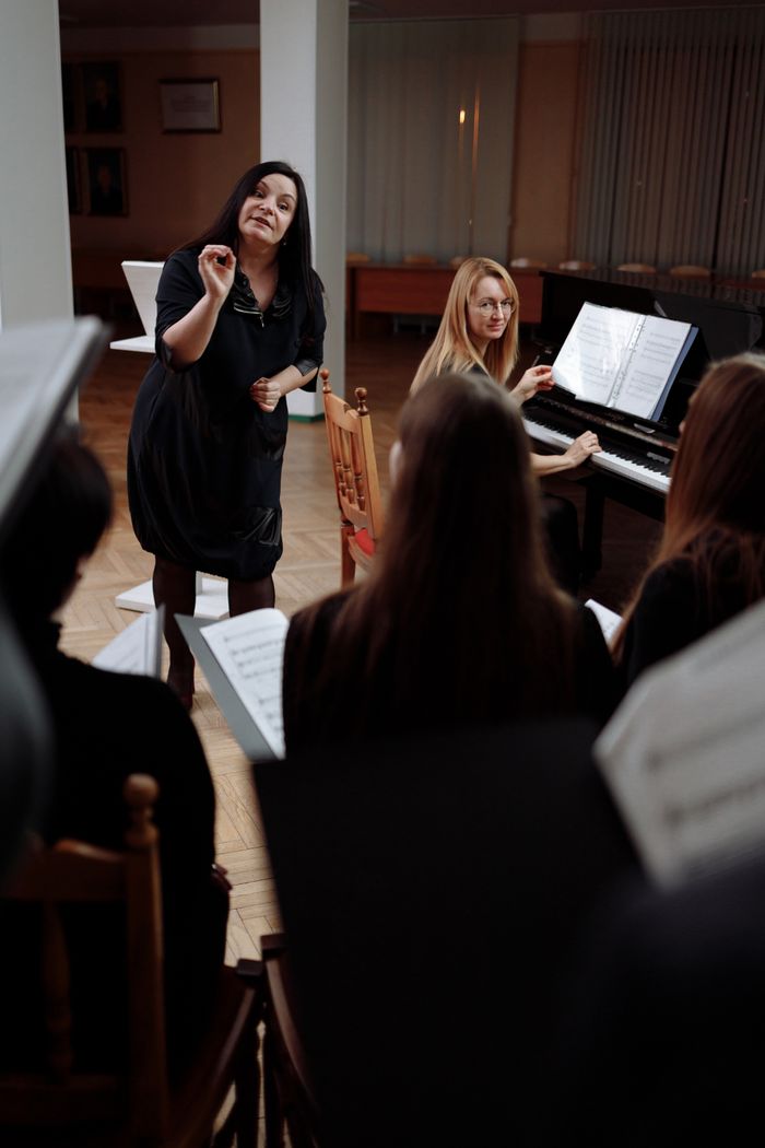 The Art of Drawing Readers In: Your attractive post title goes here A choir rehearsal indoors with a conductor leading and a pianist accompanying.